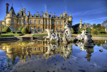 HD desktop wallpaper of Waddesdon Manor, a grand man-made palace with intricate architecture, reflected in a tranquil garden fountain under a clear blue sky.