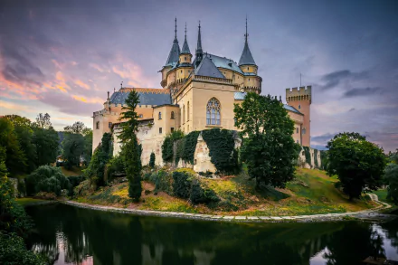 Bojnice Castle, Slovakia: historic man-made castle on a wooded island reflected in its moat at sunset — HD PC desktop wallpaper/background.