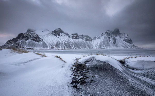 Snow-covered Vestrahorn Mountain rises under a moody winter sky in Iceland, captured in stunning 4K Ultra HD for a serene nature desktop wallpaper.