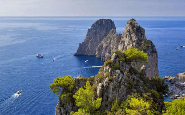HD desktop wallpaper showing the Faraglioni rock formations rising from the blue sea off Capri, Italy, with a clear sky and horizon in the background.