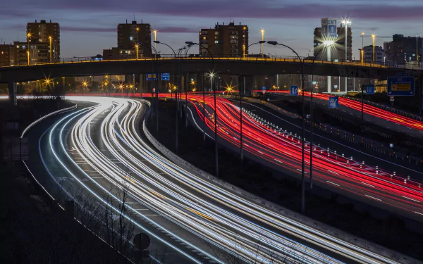 Time-lapse 4K Ultra HD photo of a busy Madrid road with light trails, city buildings, and a bridge under dusk skies in Spain.