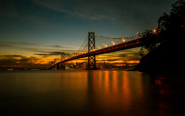 Sunset over San Francisco’s Bay Bridge in California, captured in stunning 4K Ultra HD with glowing lights reflecting on calm water.