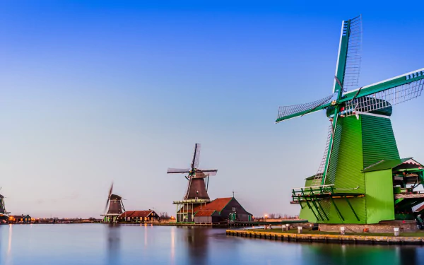 HD PC desktop background: Netherlands man-made windmills lining a calm waterfront at dusk, vivid sky and soft reflections.