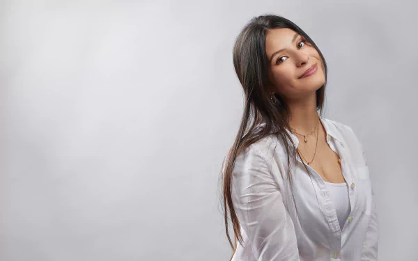 Long-haired woman model with black hair, smiling in a white blouse against a soft gray backdrop — 2K Quad HD PC desktop wallpaper/background.