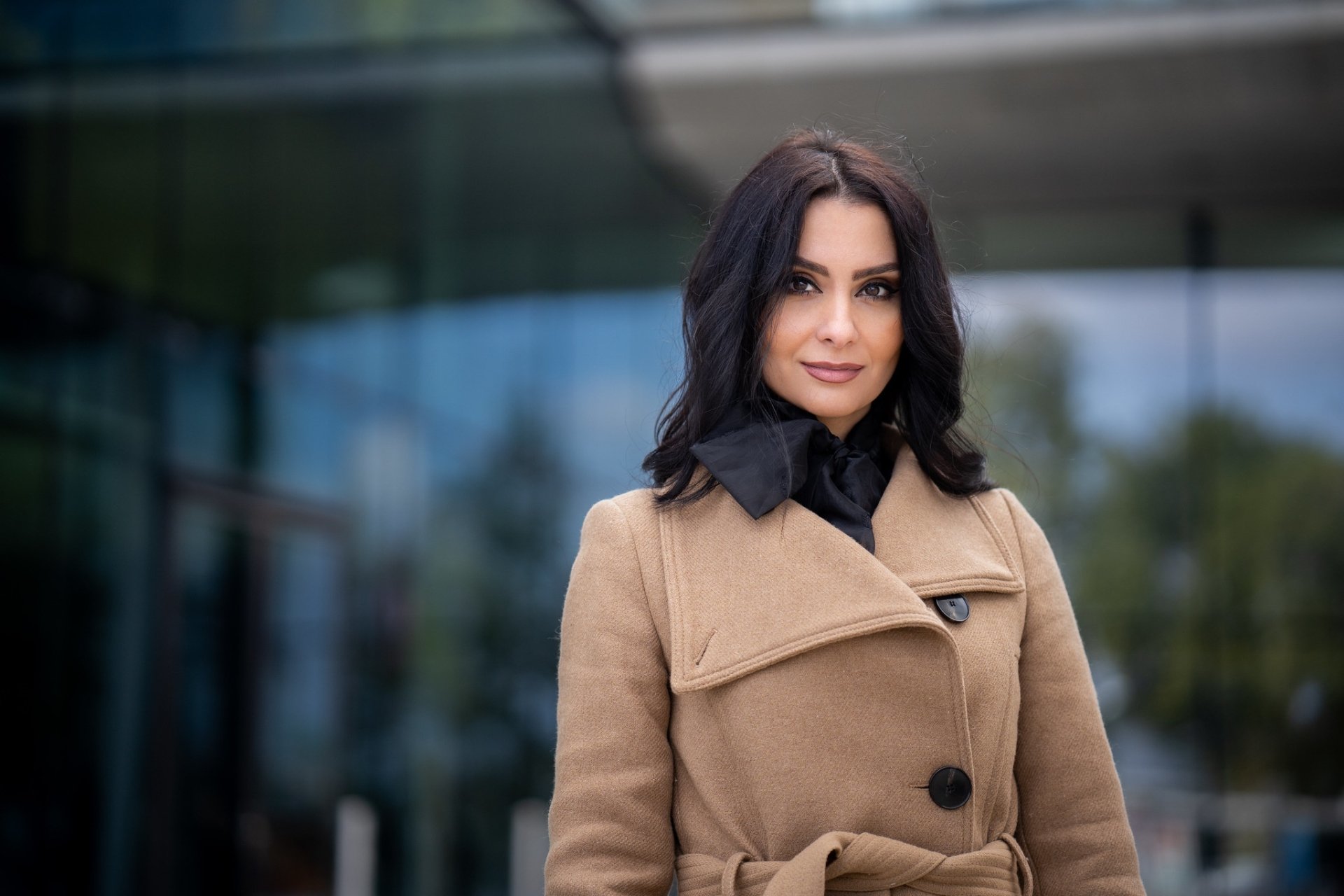 HD desktop wallpaper featuring a woman with black hair wearing a stylish coat, captured with a shallow depth of field that softly blurs the background.