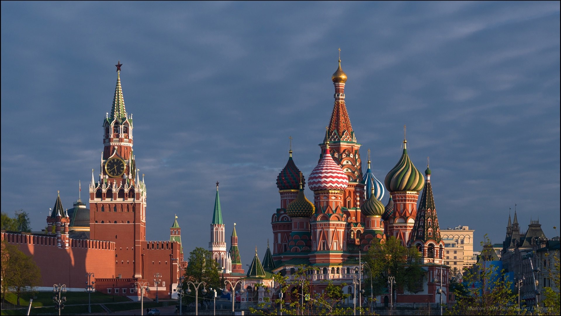 HD desktop wallpaper featuring Moscow’s Red Square with the Kremlin, Spasskaya Tower, and the colorful domes of Saint Basil's Cathedral under a dramatic sky.