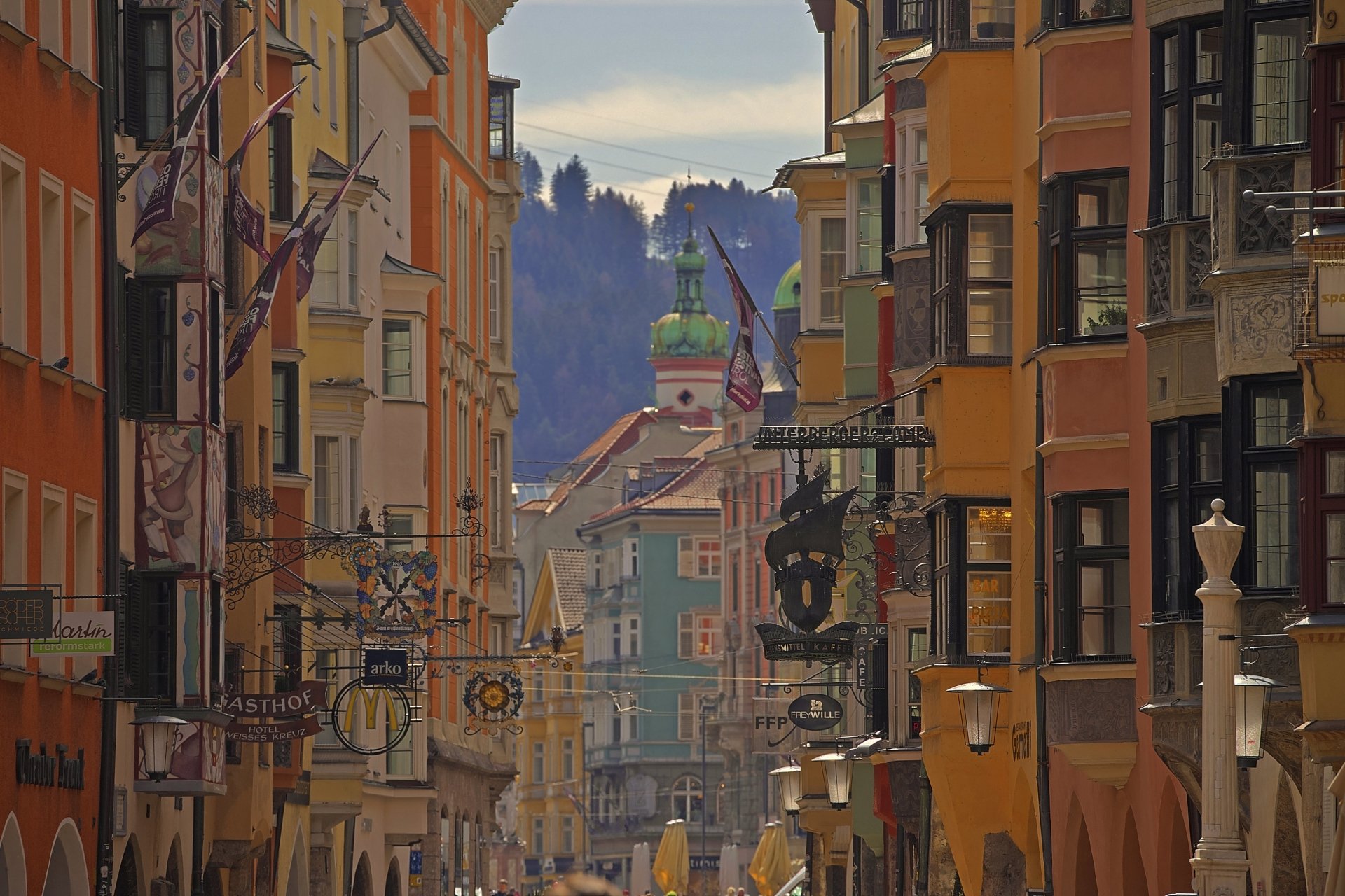 HD desktop wallpaper showcasing colorful man-made buildings and houses lining a street in Innsbruck, Austria, with mountain scenery in the background.