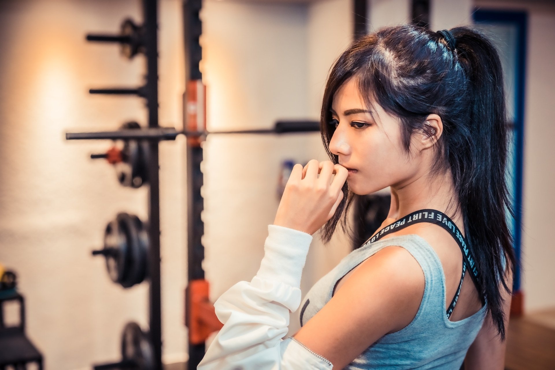 Profile of an Asian woman with black hair in a ponytail, wearing athletic wear, captured in a high-definition gym setting as a desktop wallpaper background.