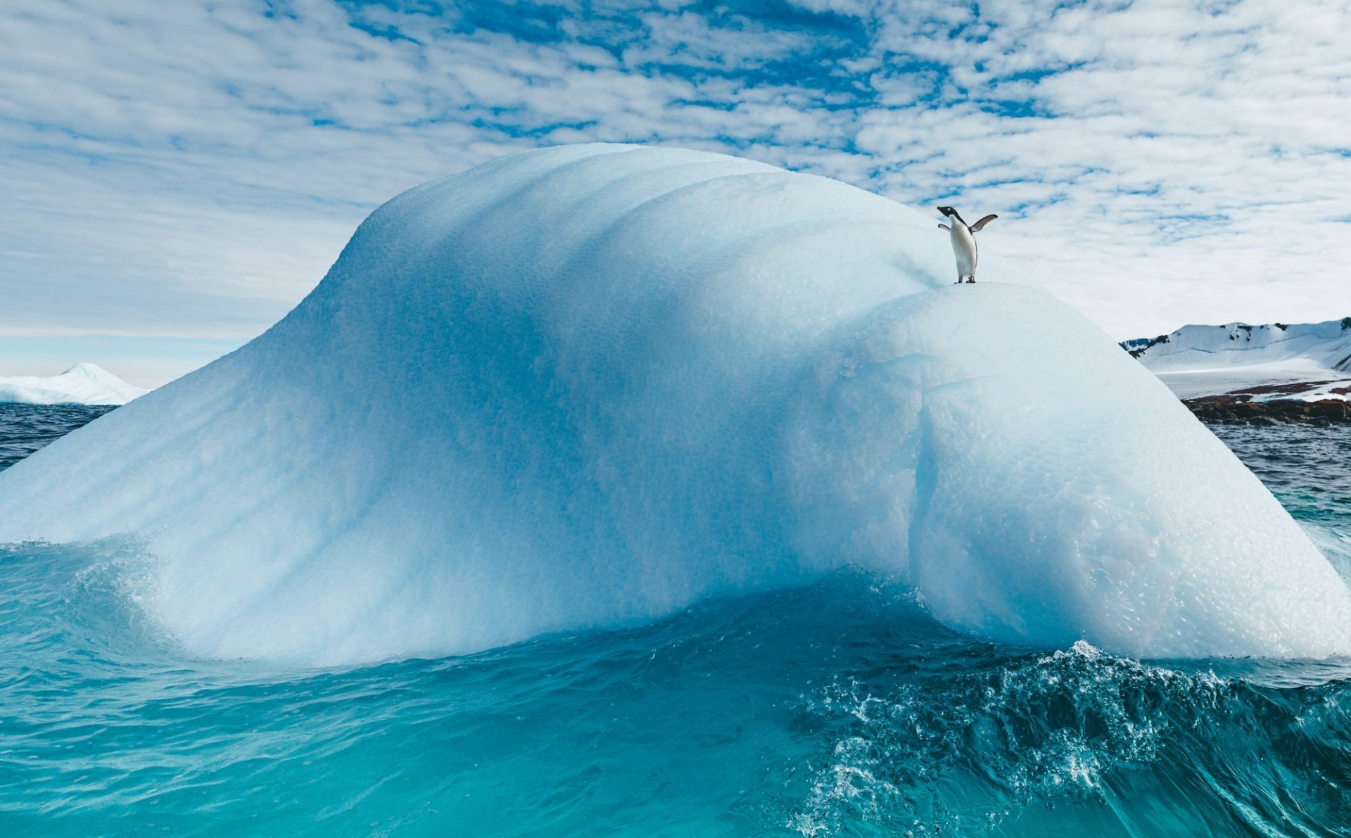 HD PC desktop wallpaper background: a penguin (bird, animal) stands on a rounded iceberg above turquoise waters beneath a cloudy sky.
