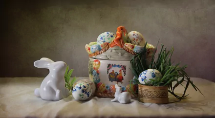 HD still life desktop wallpaper featuring an Easter-themed arrangement with a rabbit figurine, decorated eggs, a floral basket, and green foliage on a neutral background.