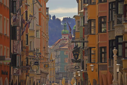 HD desktop wallpaper showcasing colorful man-made buildings and houses lining a street in Innsbruck, Austria, with mountain scenery in the background.