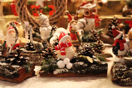 Festive Christmas market scene featuring pine cones, Santa and snowman toys, ornaments, and holiday decorations arranged on a wooden surface.