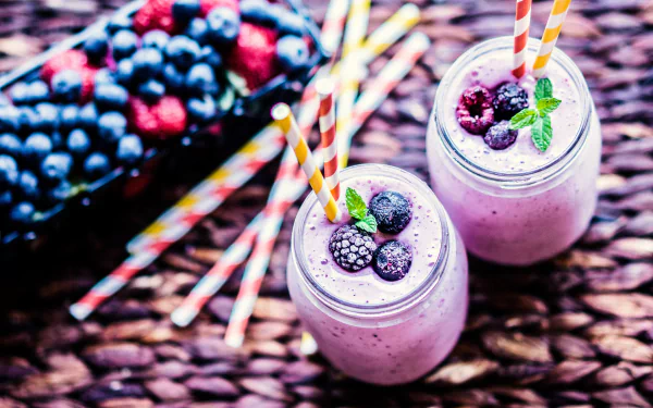4K Ultra HD PC desktop wallpaper/background of two berry smoothies (food) in glass jars with striped straws, topped with mixed berries and mint on a woven mat.
