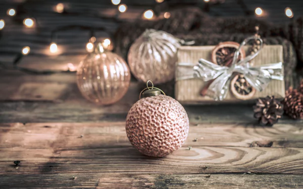 5K Ultra HD PC desktop wallpaper background: rustic wooden table with copper Christmas baubles, twinkling lights, wrapped gift and pinecones — holiday decoration scene.