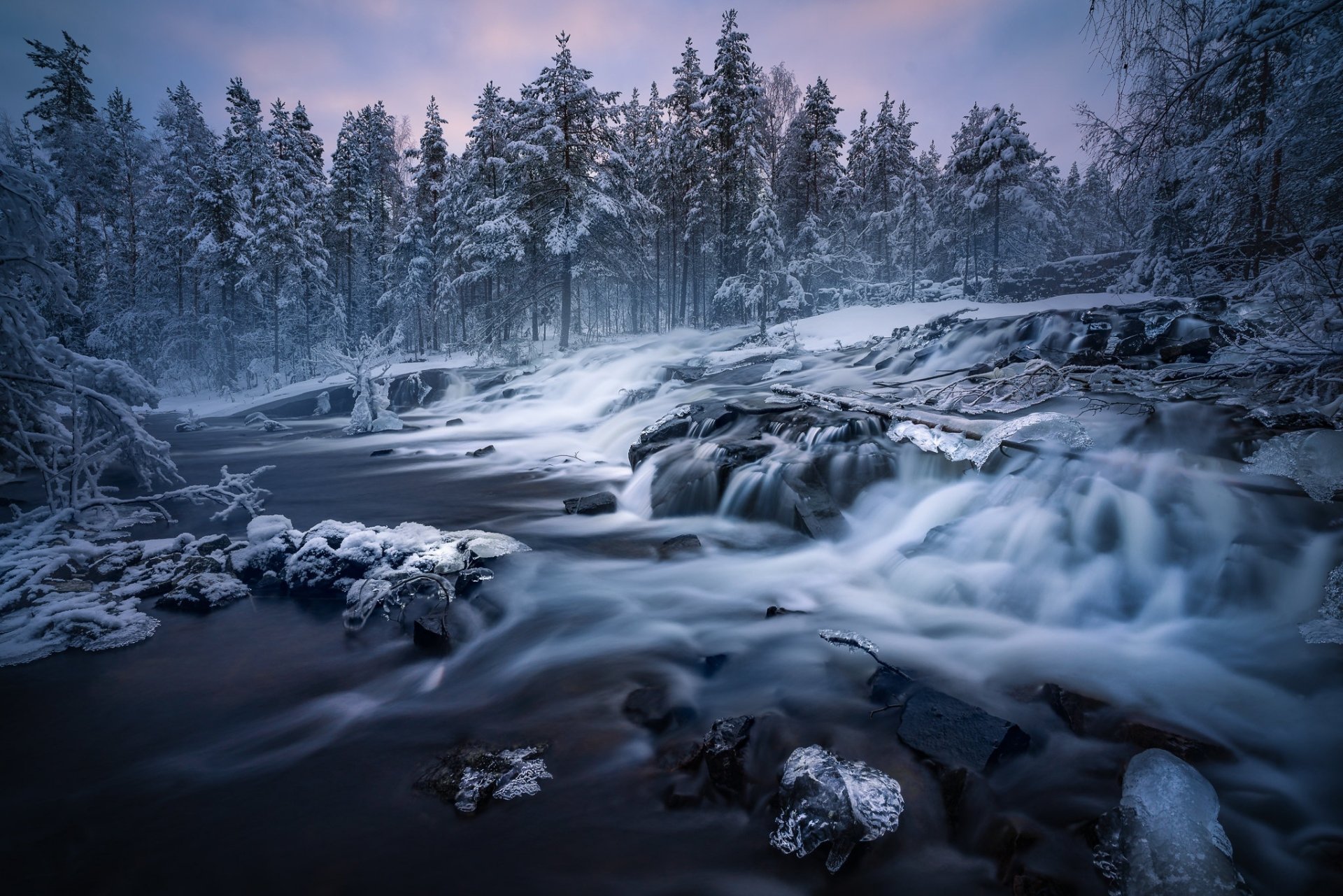 A serene winter waterfall flows through a snowy Norwegian forest along a river, captured in stunning HD for a nature-themed desktop wallpaper.