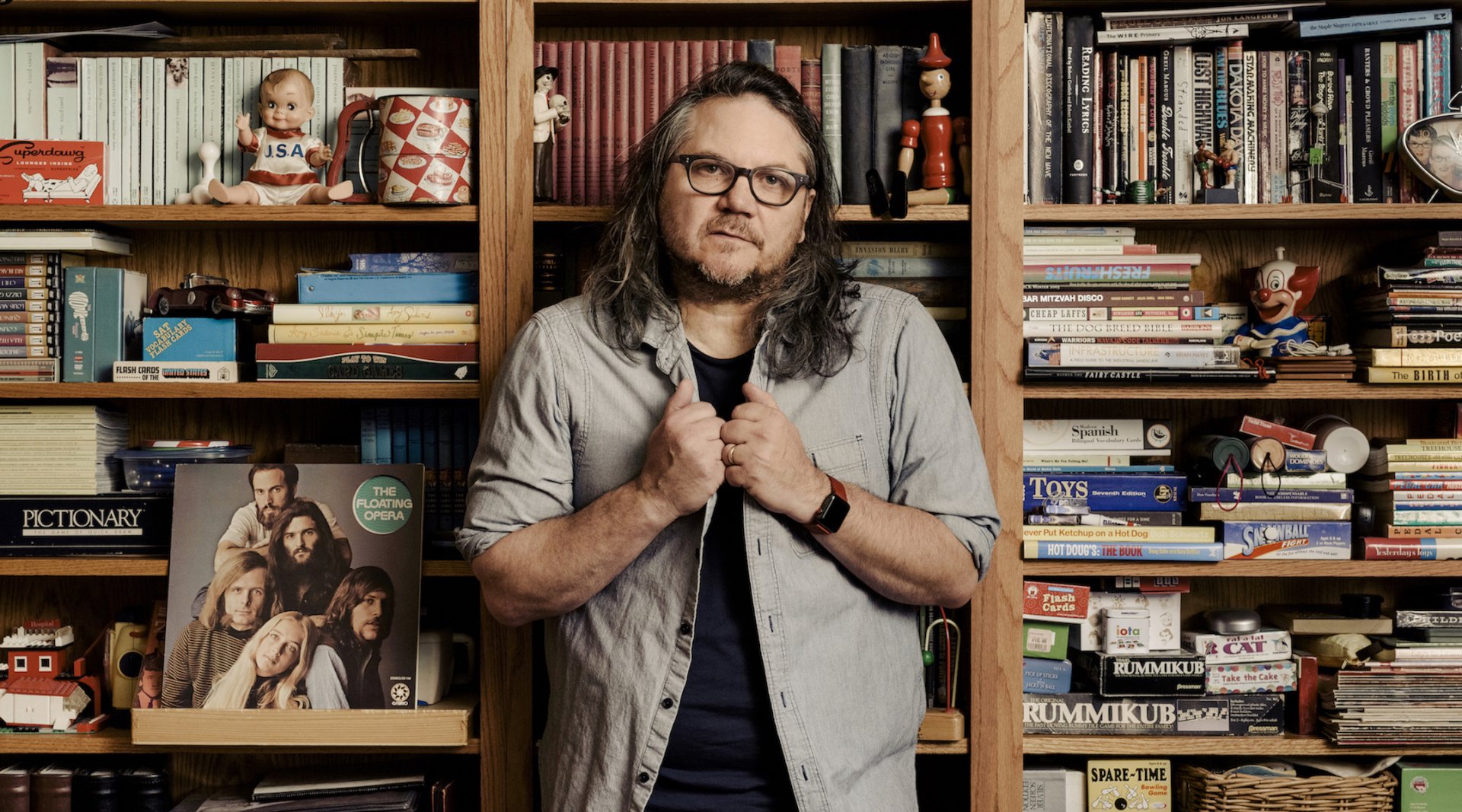 HD desktop wallpaper featuring Jeff Tweedy standing in front of a bookshelf filled with various books and objects.