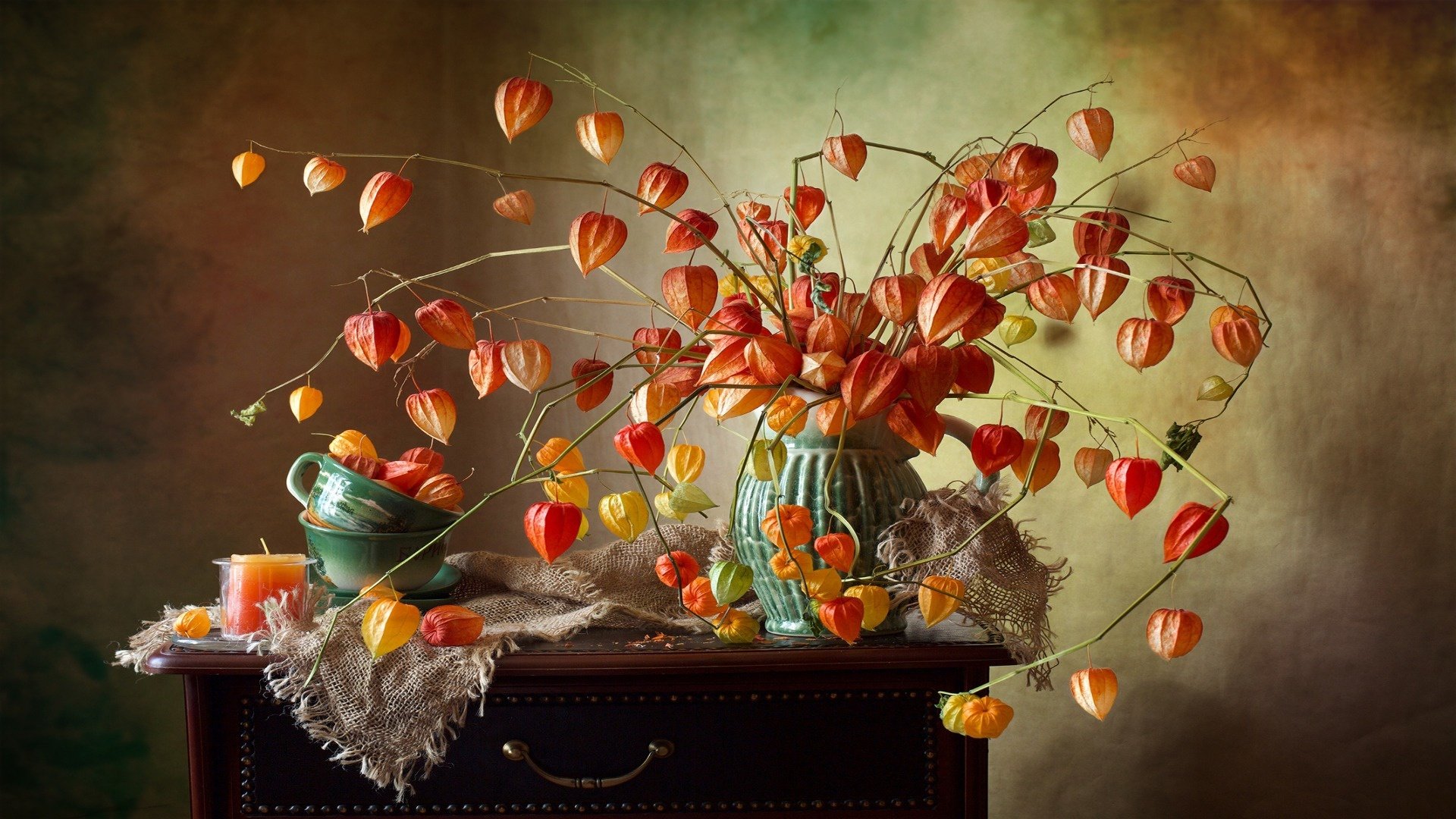 HD still life photography of a vase filled with vibrant orange flowers and lantern-like pods, set against a textured background on a dark wooden surface.