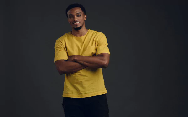 HD wallpaper of a smiling person in a yellow shirt with crossed arms against a grey background.