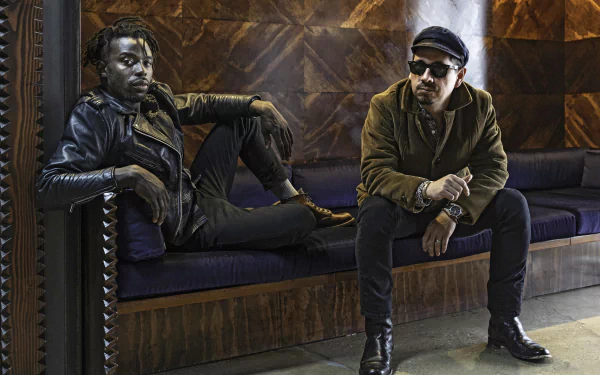 HD desktop wallpaper featuring two members of the Black Pumas band seated casually in a stylish interior setting.