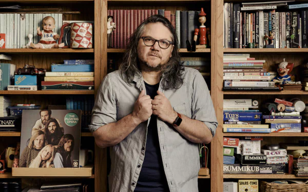 HD desktop wallpaper featuring Jeff Tweedy standing in front of a bookshelf filled with various books and objects.