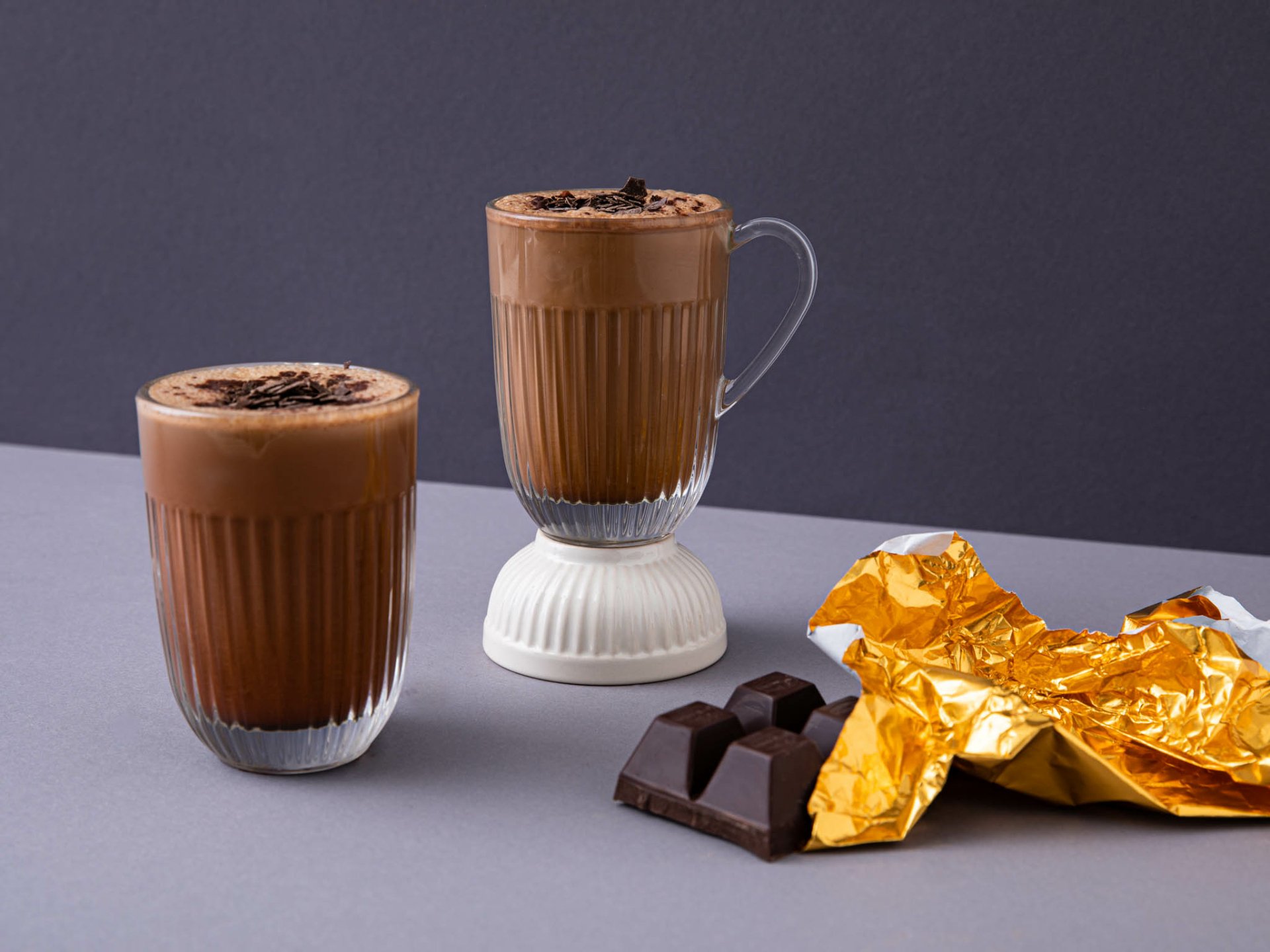 HD desktop wallpaper of two glasses of coffee with chocolate sprinkles and chocolate pieces wrapped in golden foil.