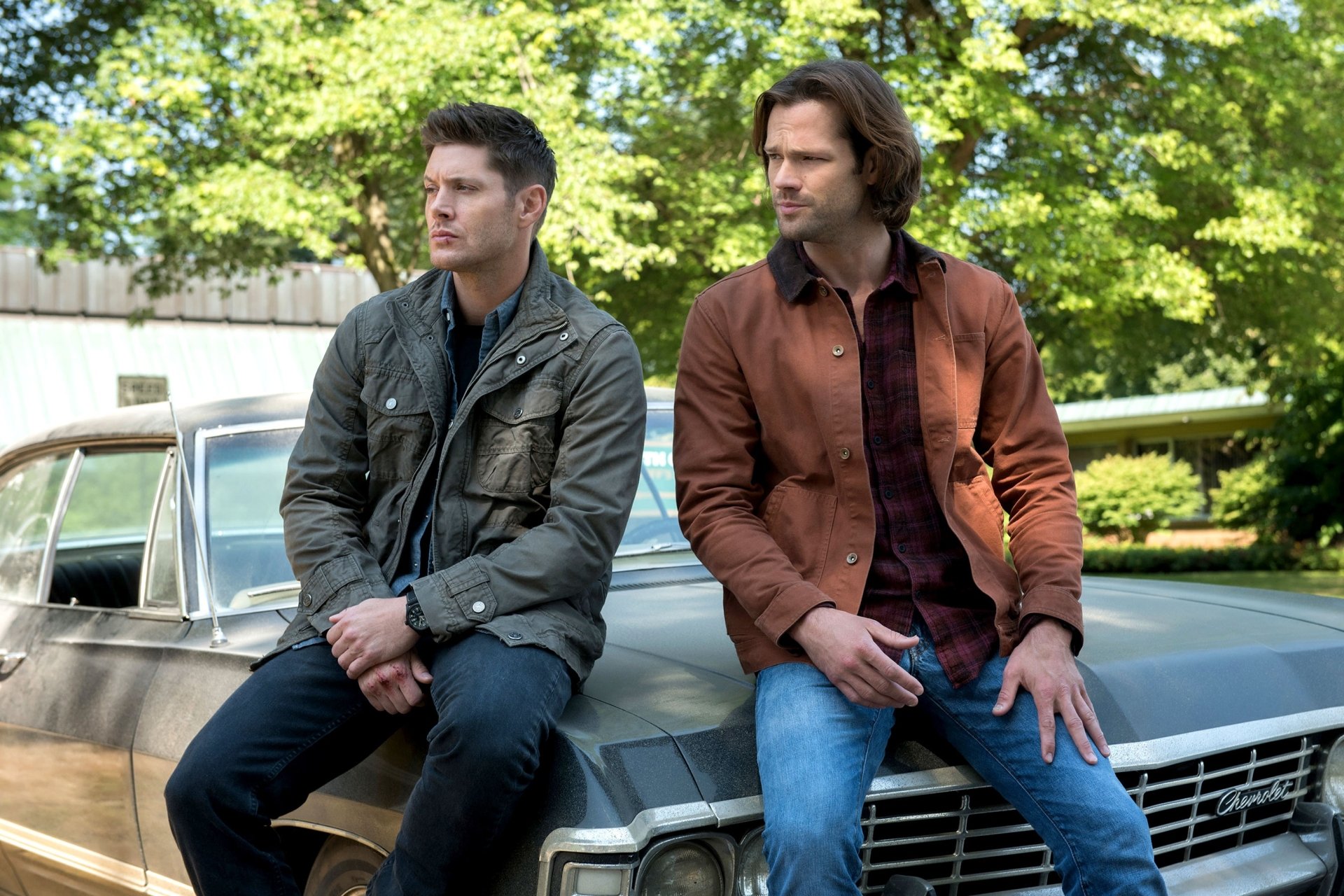 HD PC desktop wallpaper featuring Jared Padalecki as Sam Winchester and Jensen Ackles as Dean Winchester from the TV show Supernatural, sitting on a classic car outdoors.