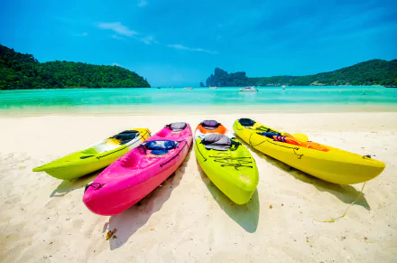 HD wallpaper of colorful kayaks on a sunny beach with clear blue water and a scenic backdrop.