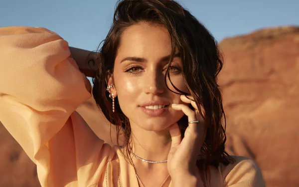 Portrait of Cuban actress Ana de Armas with green eyes and brunette hair, captured in a 4K Ultra HD desktop wallpaper against a sunlit rocky background.