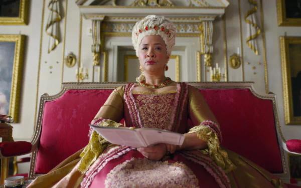 HD desktop wallpaper from Bridgerton featuring a character dressed in regal attire, sitting on a red throne in an ornate room.