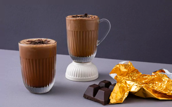 HD desktop wallpaper of two glasses of coffee with chocolate sprinkles and chocolate pieces wrapped in golden foil.