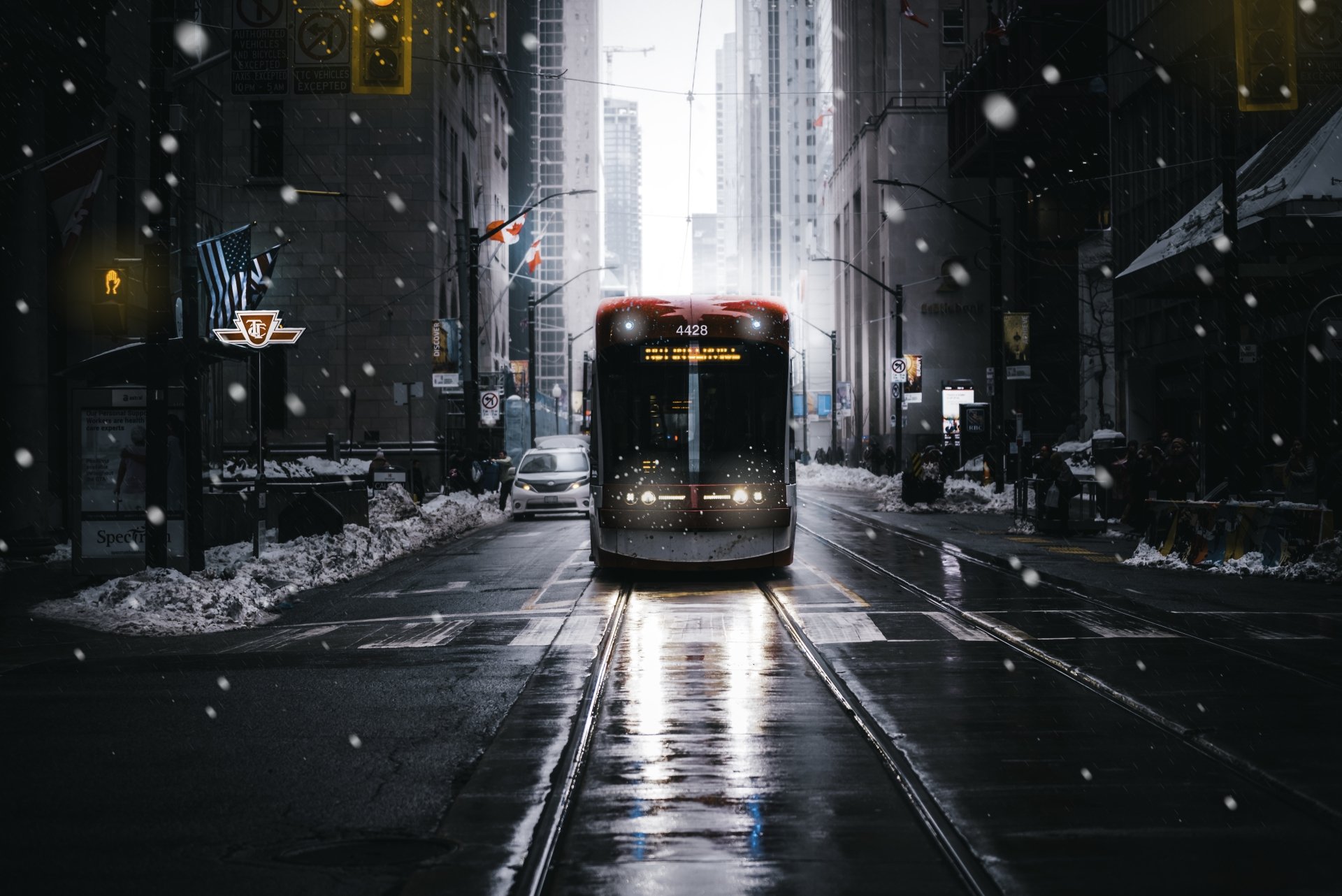 A 4K Ultra HD PC desktop wallpaper featuring a tram traveling down snowy city streets at dusk, with tall buildings and glowing streetlights creating an urban winter scene.