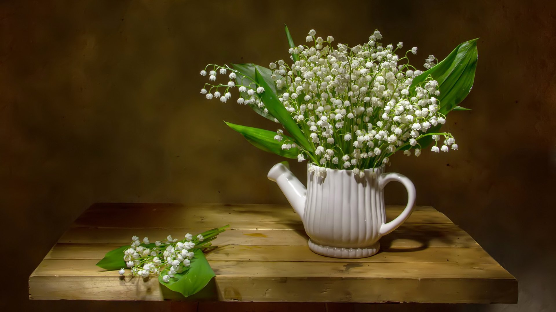 HD PC desktop wallpaper featuring a still life photograph of delicate white lily of the valley flowers arranged in a white ceramic pitcher on a wooden table.
