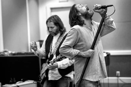 HD wallpaper featuring The Black Crowes with one member singing into a microphone and another playing guitar, in monochrome.
