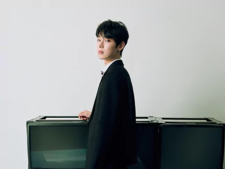 2K Quad HD PC desktop wallpaper: young man in a dark coat standing beside stacked monitors, minimalist music-themed portrait.