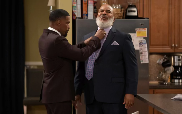 A scene from Dad Stop Embarrassing Me with a man adjusting another man's tie in a home kitchen, capturing a heartwarming father-son moment for HD desktop wallpaper.