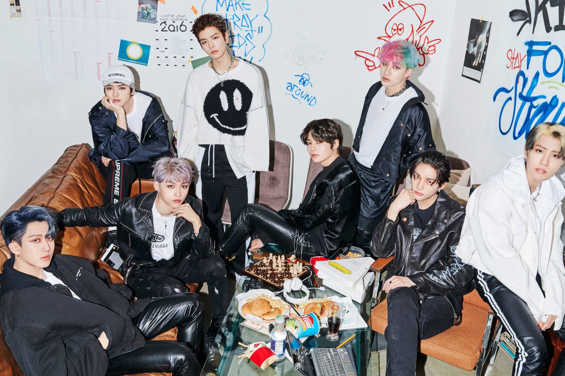 HD PC desktop wallpaper featuring the K-pop boy band Stray Kids posing together in a room filled with graffiti and casual decor.