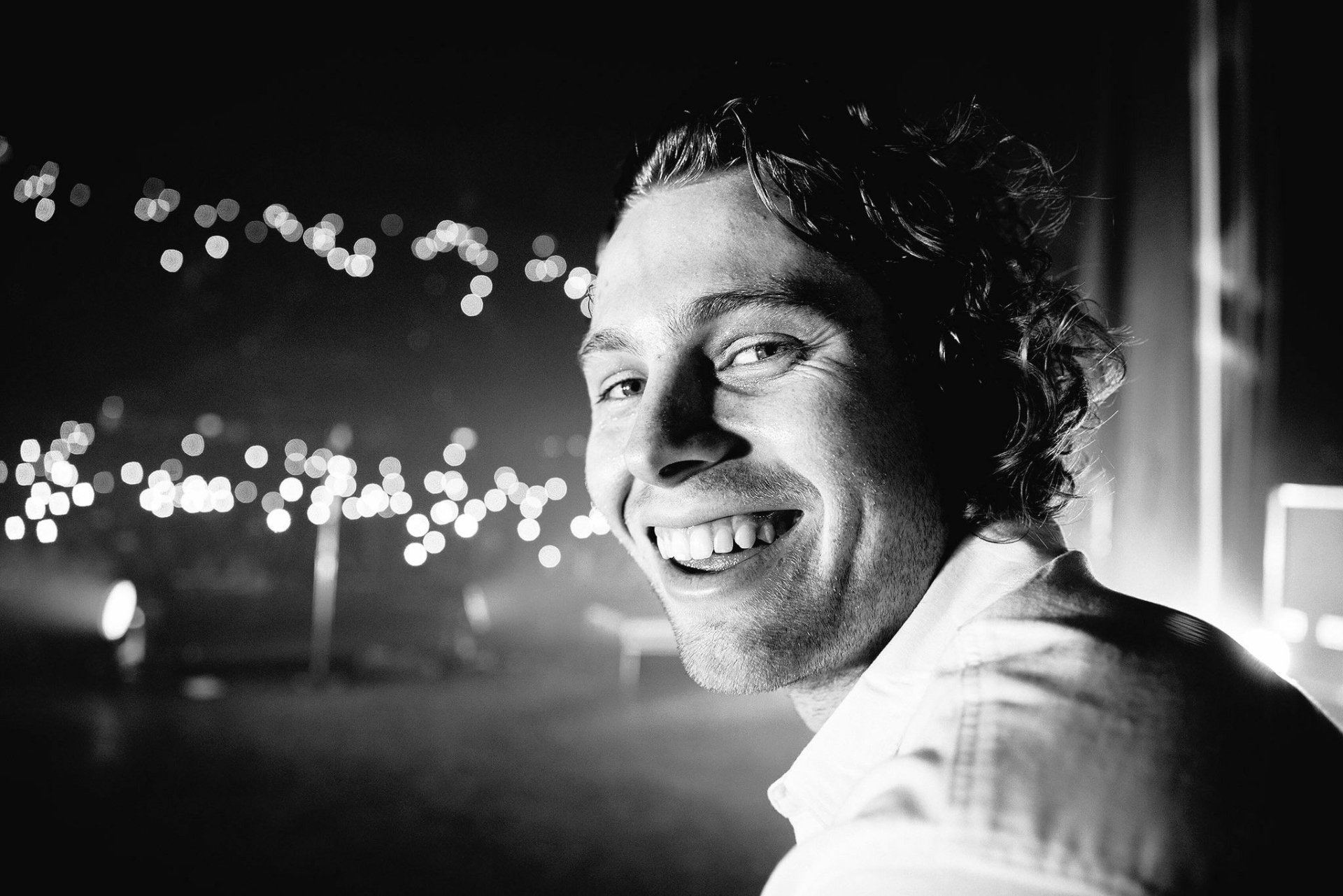 A joyful black-and-white portrait of Luke Hemmings, smiling with lights twinkling in the background, making it a striking HD desktop wallpaper for music lovers.