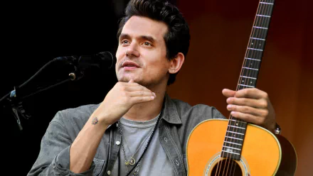 A close-up of John Mayer performing with his acoustic guitar, showcasing his expressive gesture and passion for music. This HD image serves as a vibrant desktop wallpaper.
