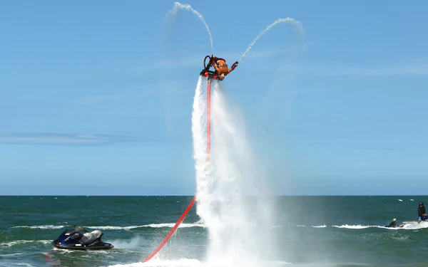 Person performing flyboard water sports with high jet stream propulsion over the ocean as HD desktop wallpaper