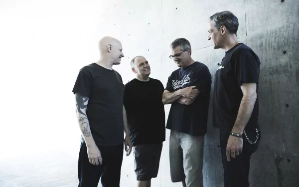A group of four musicians from the band Descendents, dressed in black, engage in conversation against a minimalistic, light background. This HD wallpaper captures the essence of their music.