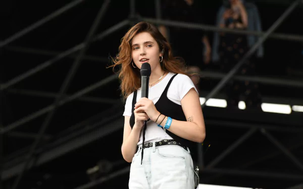 Clairo performs on stage, microphone in hand, wearing a casual outfit. This HD image captures a vibrant moment in music, making it a striking desktop wallpaper.