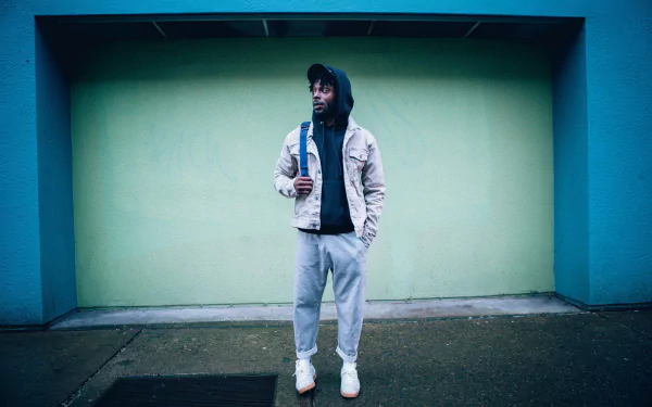HD desktop wallpaper featuring Isaiah Rashad standing in front of a teal wall, exuding a cool, effortless vibe.