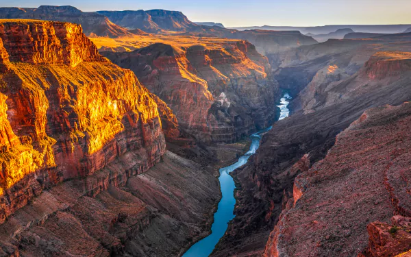 Sunlit Grand Canyon vista at golden hour, deep red-rock cliffs and a winding blue Colorado River — 5K Ultra HD PC desktop wallpaper and nature canyon background.