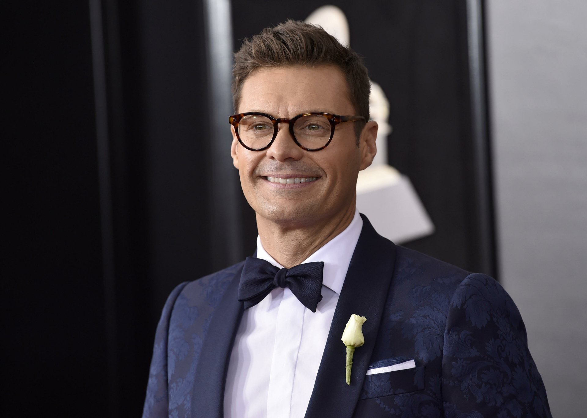 HD desktop wallpaper featuring celebrity Ryan Seacrest, smiling confidently in a stylish outfit with a bow tie and glasses, set against a glamorous background.