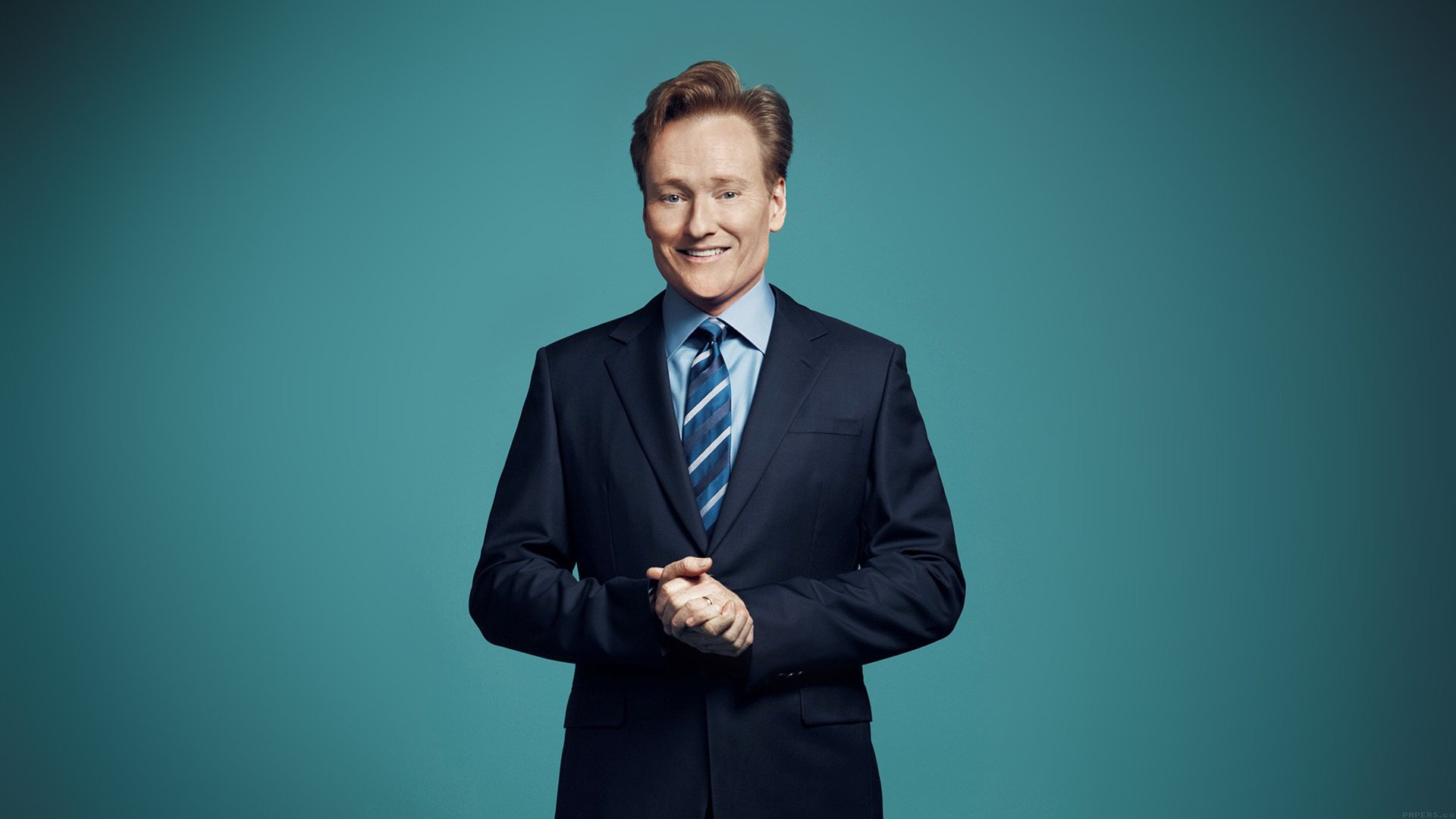 HD wallpaper of a smiling man in a suit with a teal background.