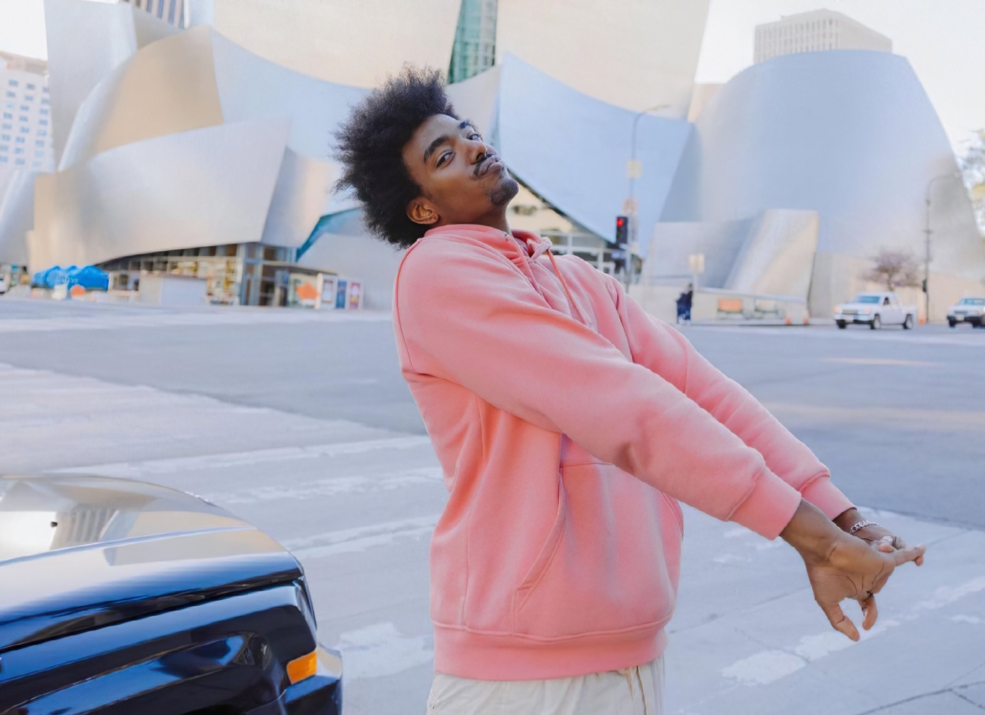 HD desktop wallpaper featuring a person in a pink hoodie stretching on an urban street with unique architecture in the background.
