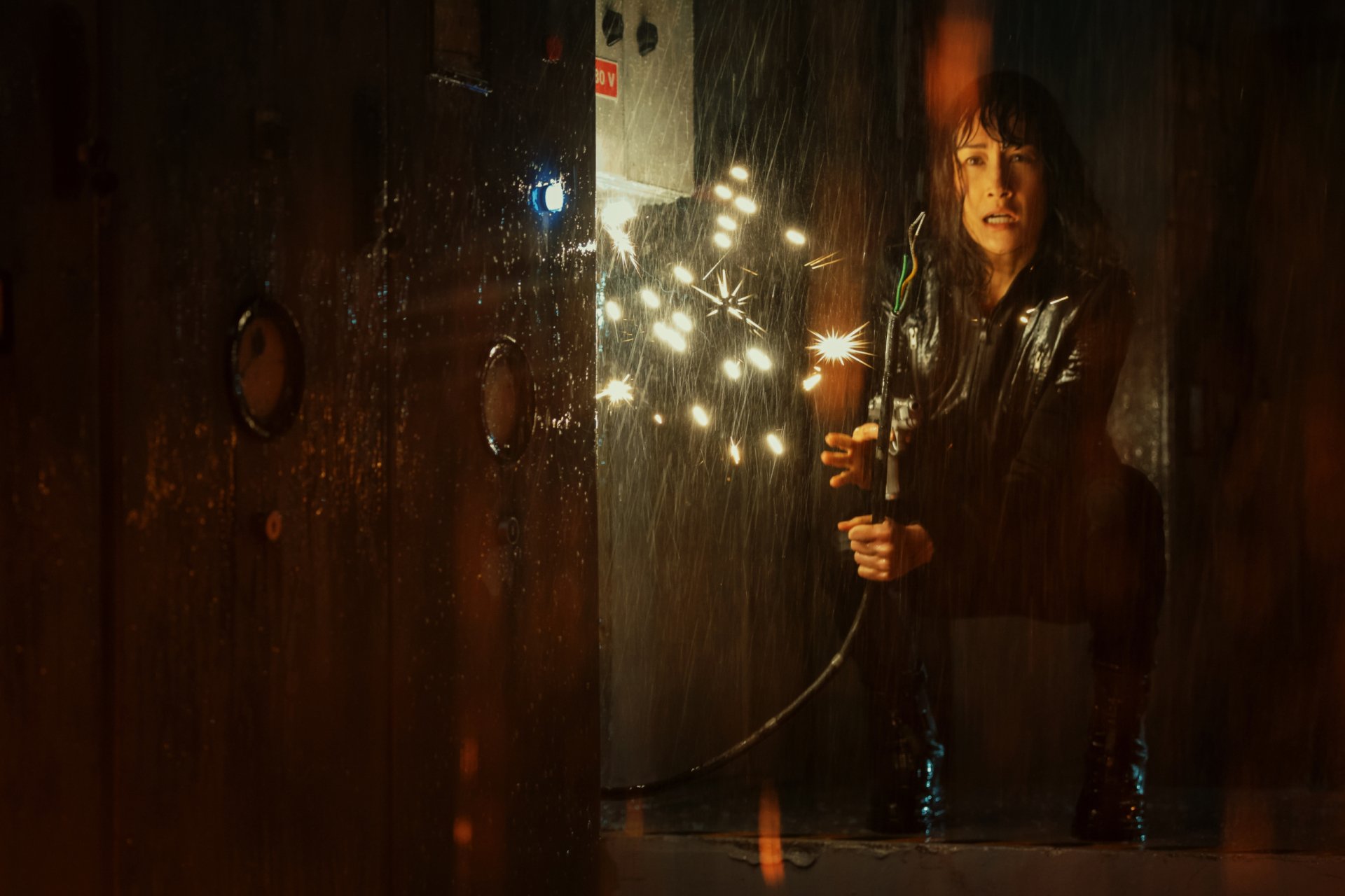 HD PC desktop wallpaper featuring Maggie Q in a dark, intense scene from the movie The Protégé, holding a lit sparkler in a dimly lit setting.