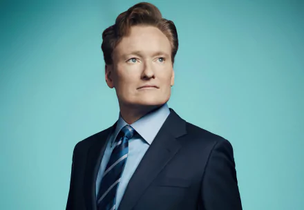 A high-definition desktop wallpaper featuring comedian Conan O'Brien, dressed in a suit, looking confidently to the side against a vibrant blue background.