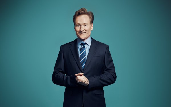 Smiling man in a dark suit and blue striped tie posing against a teal background, suitable for an HD desktop wallpaper and background.
