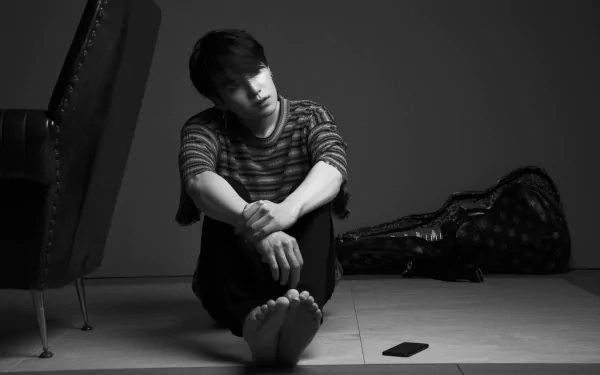 Black-and-white 4K Ultra HD wallpaper of K-pop singer Suga (Min Yoongi) from BTS sitting barefoot on the floor, with a guitar case and smartphone nearby.